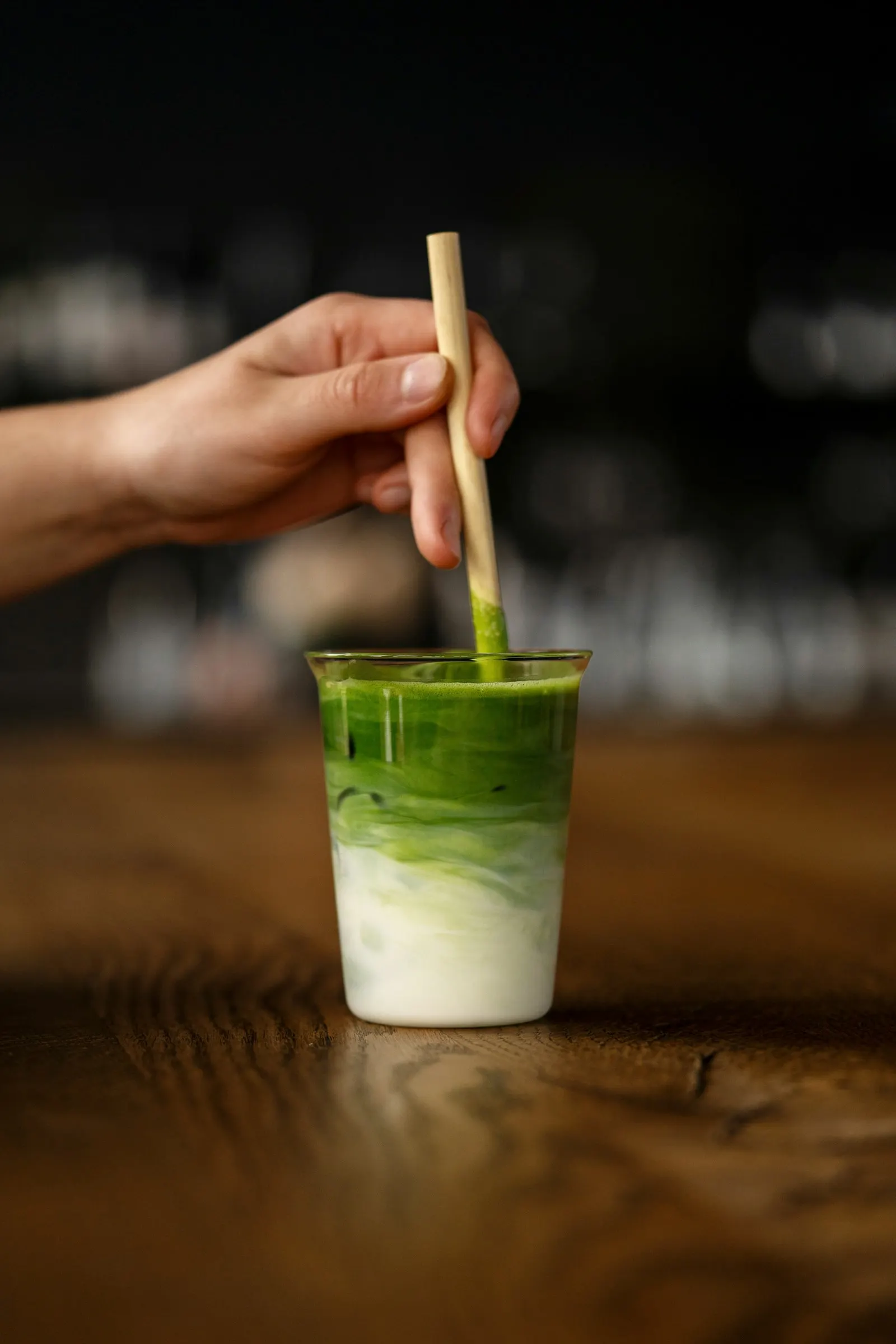 Hand stirring an iced matcha latte in a clear to-go cup